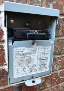 Open AC disconnect box mounted on brick wall showing pullout switch