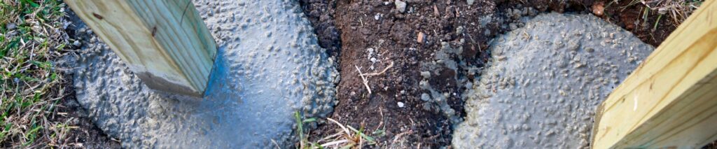 wooden fence post set in concrete in a freshly dug post hole