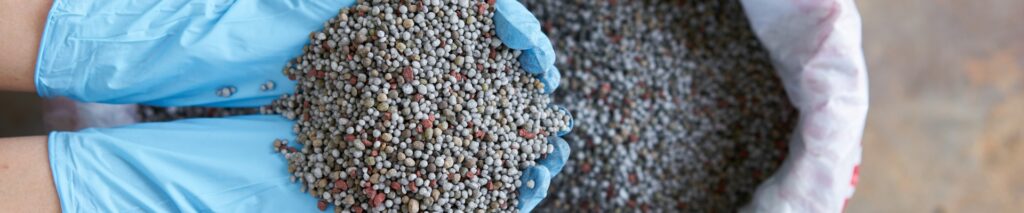 hands holding granular fertilizer over a bag for fertilizer calculator