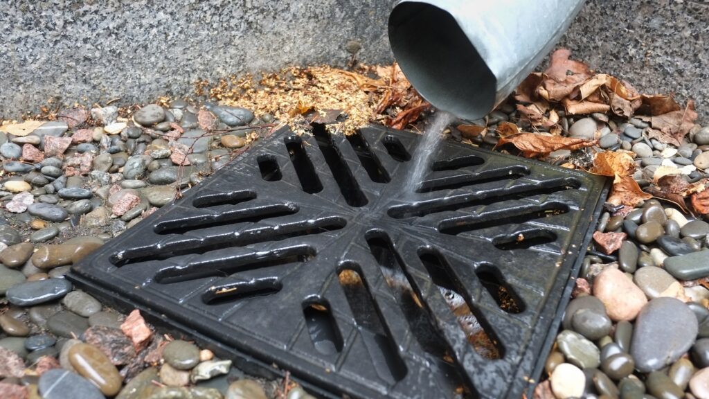 downspout discharging into a catch basin drain surrounded by gravel