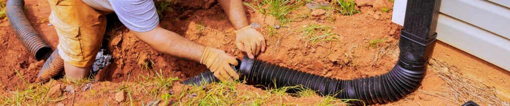 how to extend downspouts away from house — person installing buried drain pipe along foundation