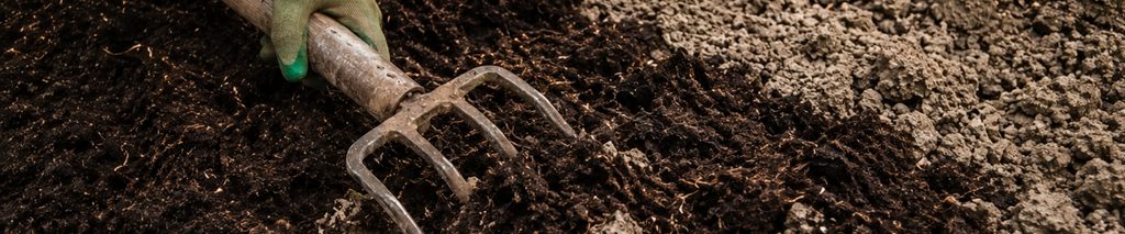 how to improve clay soil — gardener working compost into heavy clay garden bed with a garden fork