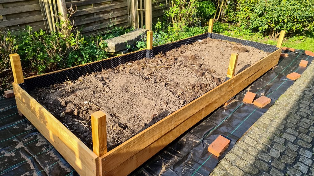 raised garden bed frame under construction with cedar lumber and corner stakes