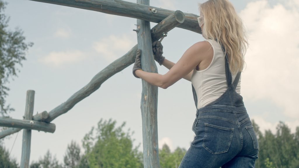 woman in overalls installing a pergola post during backyard pergola construction