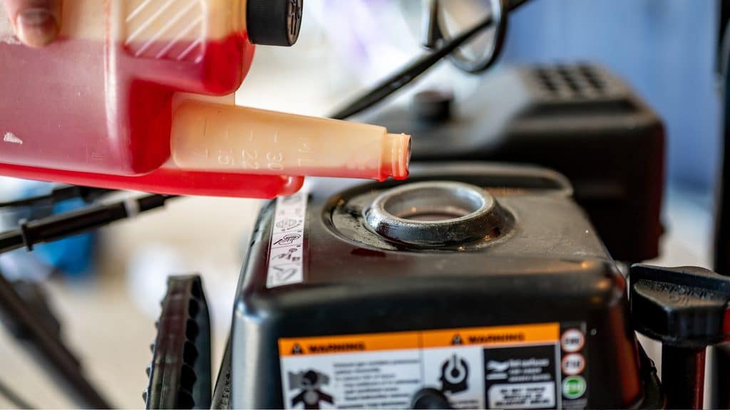 pouring fuel stabilizer into a lawn mower gas tank before winter storage
