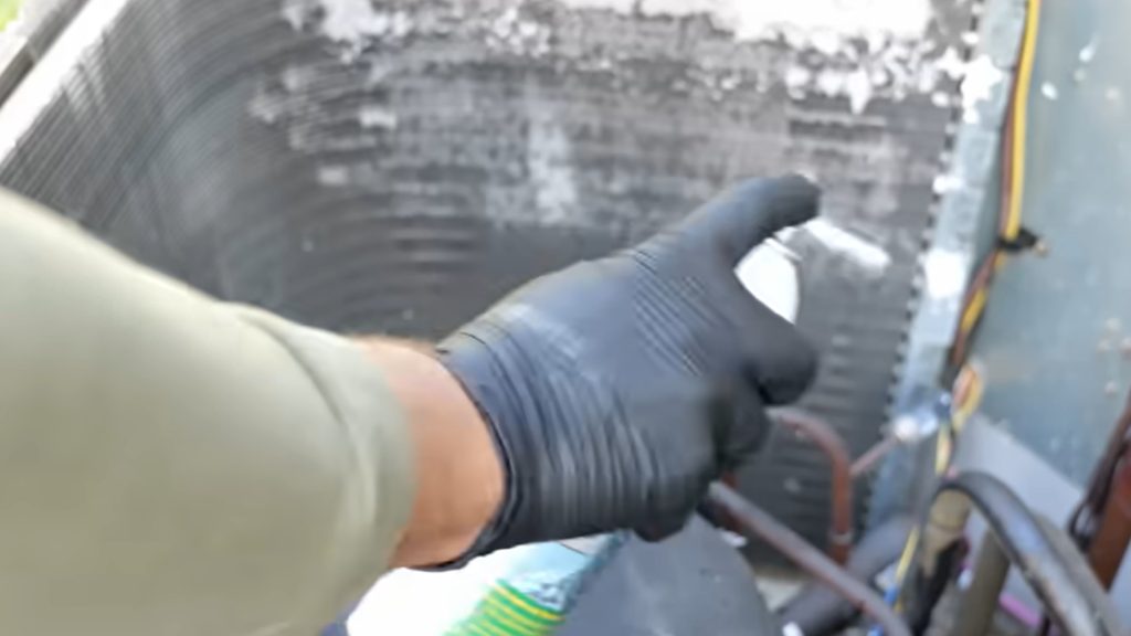 Gloved hand spraying foam coil cleaner inside an open AC condenser unit