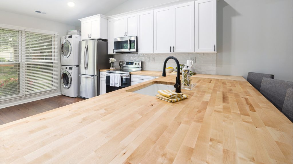 Butcher block wood countertop on a kitchen island in a bright white modern kitchen