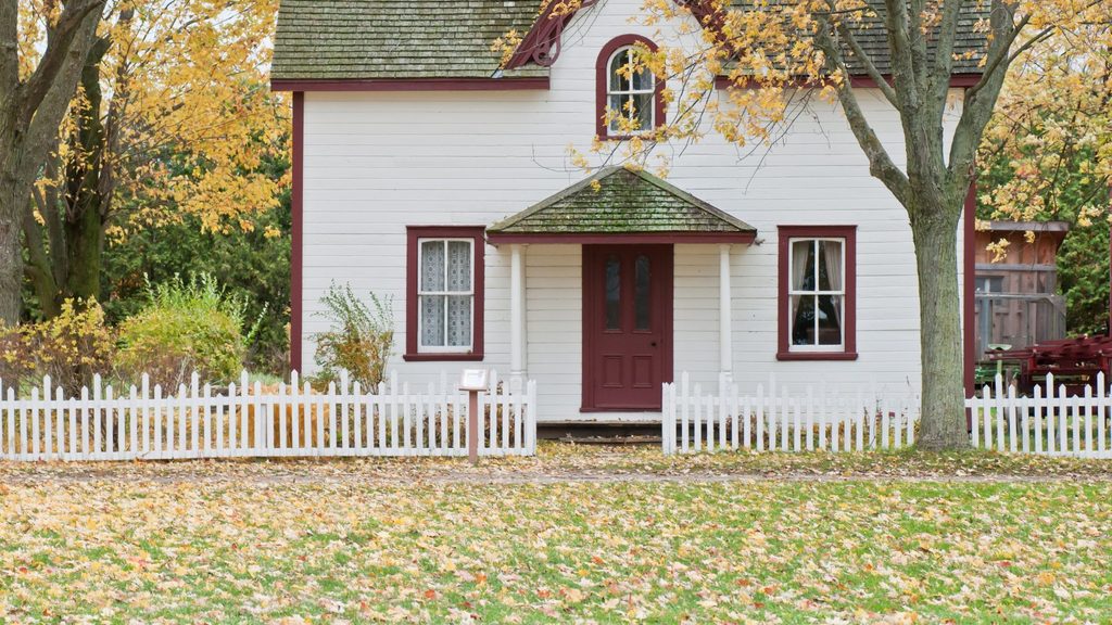 white house surrounded by fall foliage during autumn yard cleanup season