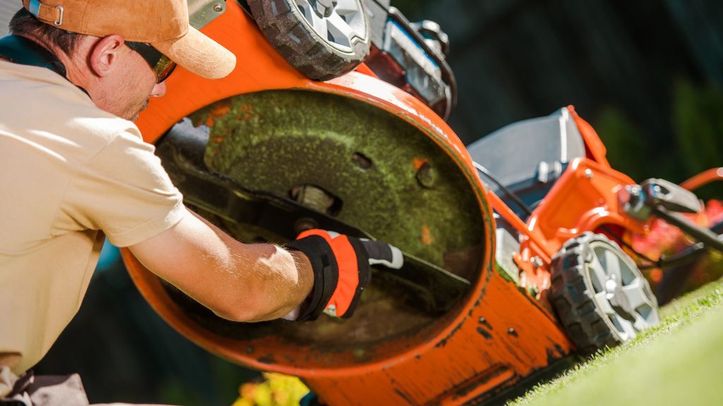 homeowner inspecting and cleaning lawn mower blade as part of fall winterization maintenance