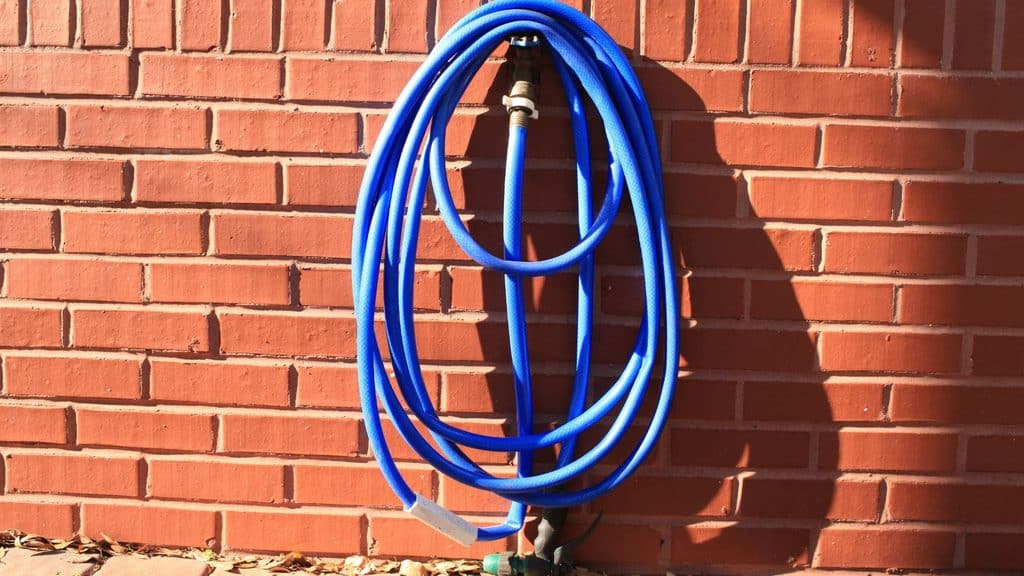 garden hose coiled and left connected to outdoor faucet on a brick wall