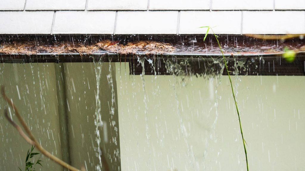 water overflowing over the edge of a clogged gutter during rain — sign gutters need cleaning