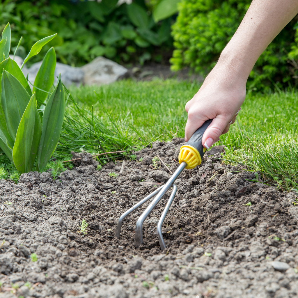 Hand using a small garden hand rake in soil — not the right tool for raking leaves off a lawn