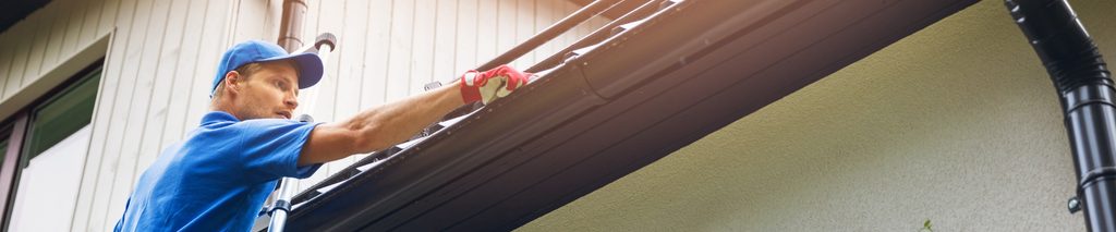 how to clean gutters — man on ladder cleaning leaves and debris from residential gutters