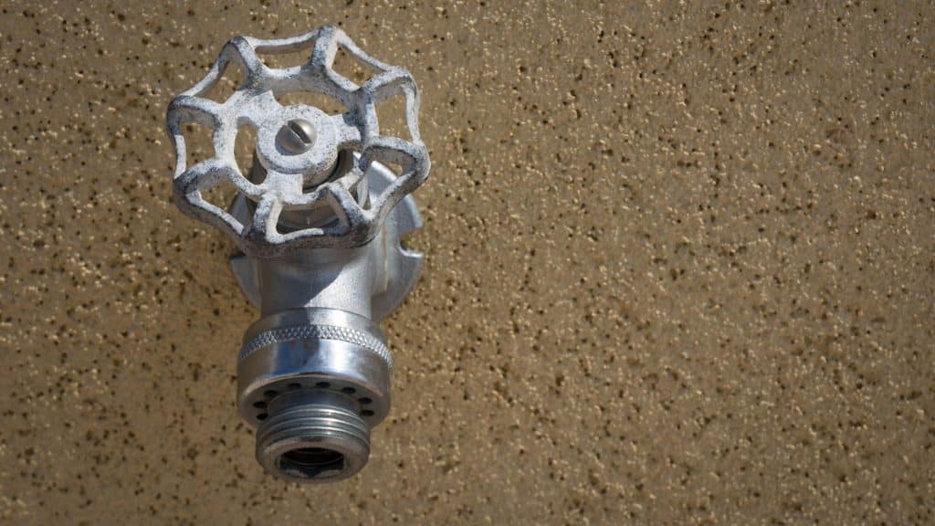 old weathered outdoor hose bib with corroded handle on a stucco wall