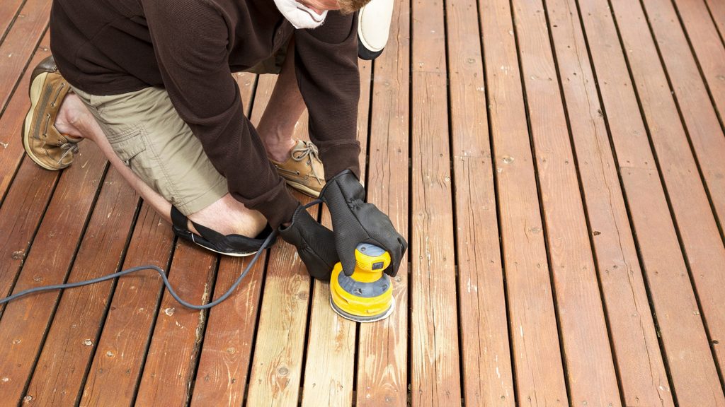 Person using an orbital sander on wood deck boards during deck restoration