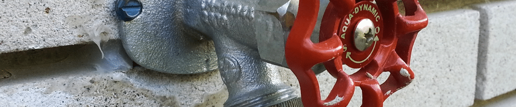 outdoor hose bib with red handle and caulked flange on a block wall with garden hose attached. How to replace a hose bib