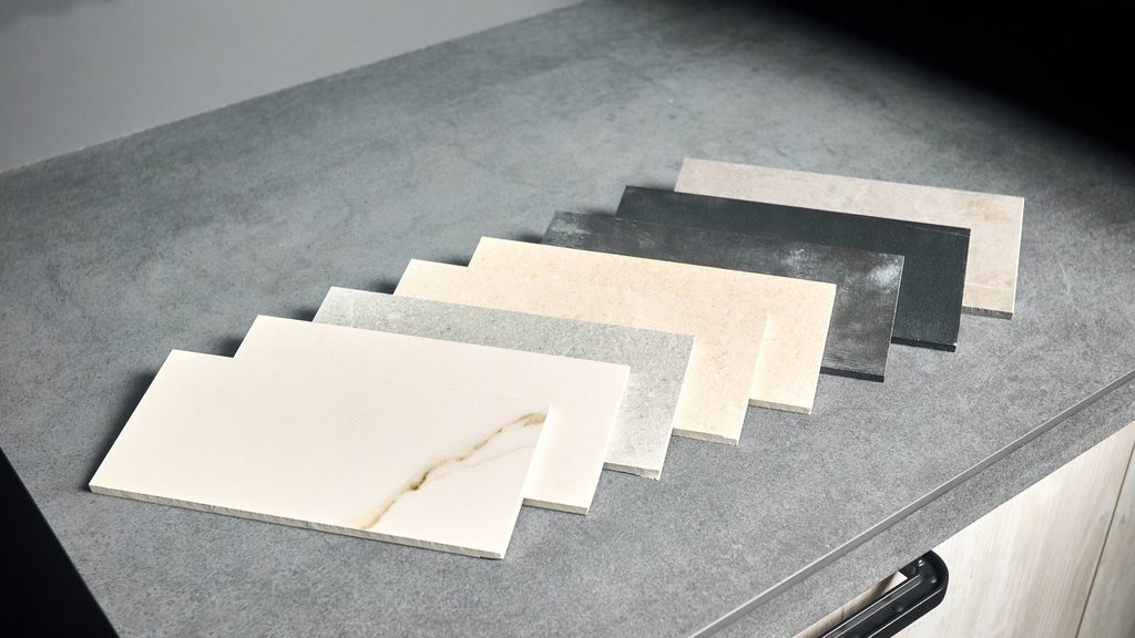 Fanned porcelain tile samples in varying gray and cream tones displayed on a dark surface