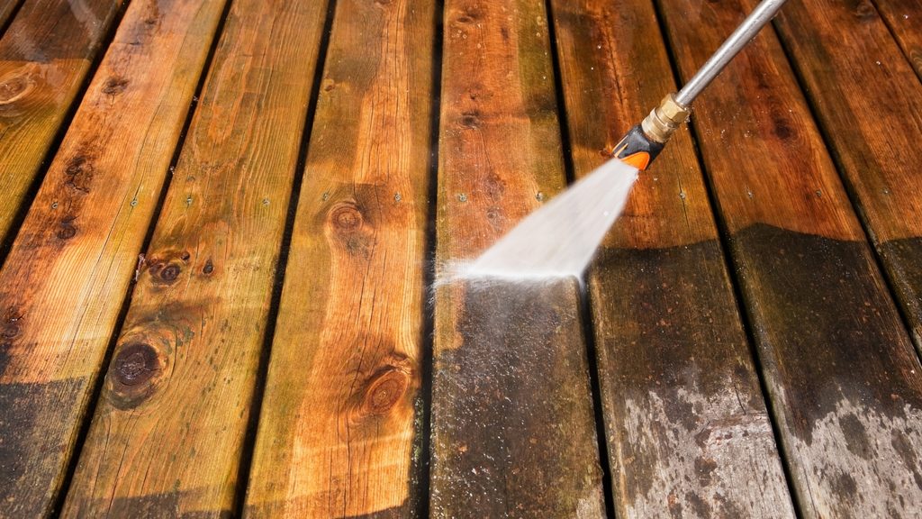 Pressure washer cleaning wood deck boards with water spraying across the surface