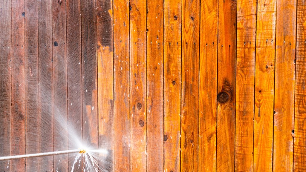 Pressure washer cleaning a wood picket fence showing the dirt and weathering being removed from the boards