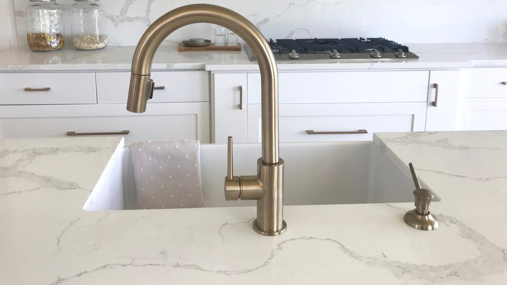 White quartz countertop with gray veining in a bright kitchen with a gold faucet and matching backsplash