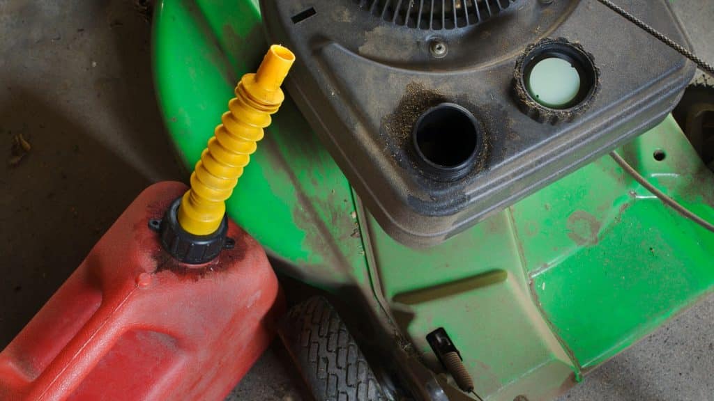 red gas can with yellow spout refilling a green lawn mower with fresh gas