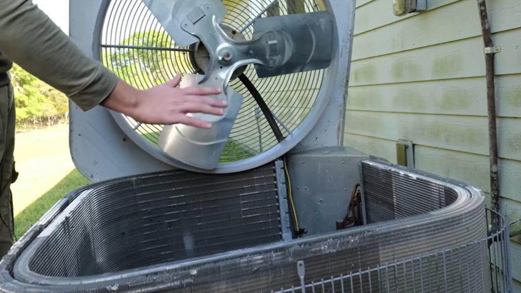 Person lifting the lid off an outdoor AC condenser unit to access the coils inside
