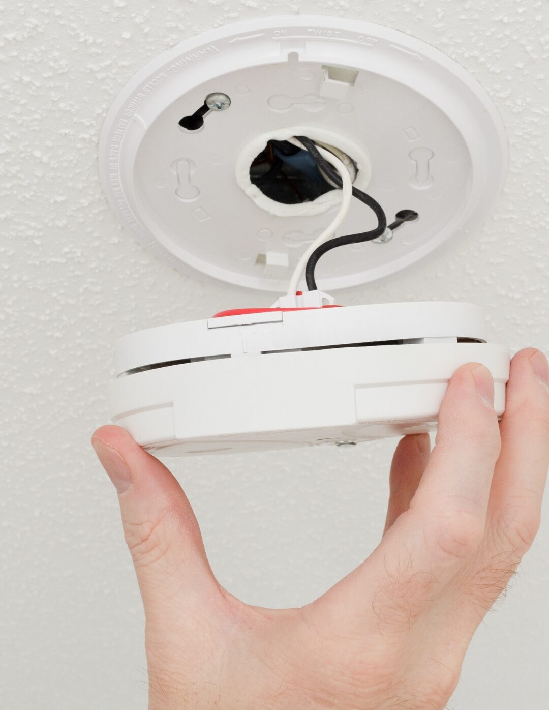 Hand twisting a smoke detector off its ceiling mount during replacement