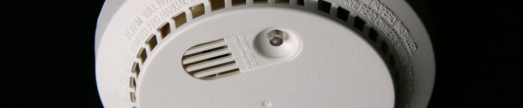 White smoke detector against a dark background in an article called how to replace smoke detectors
