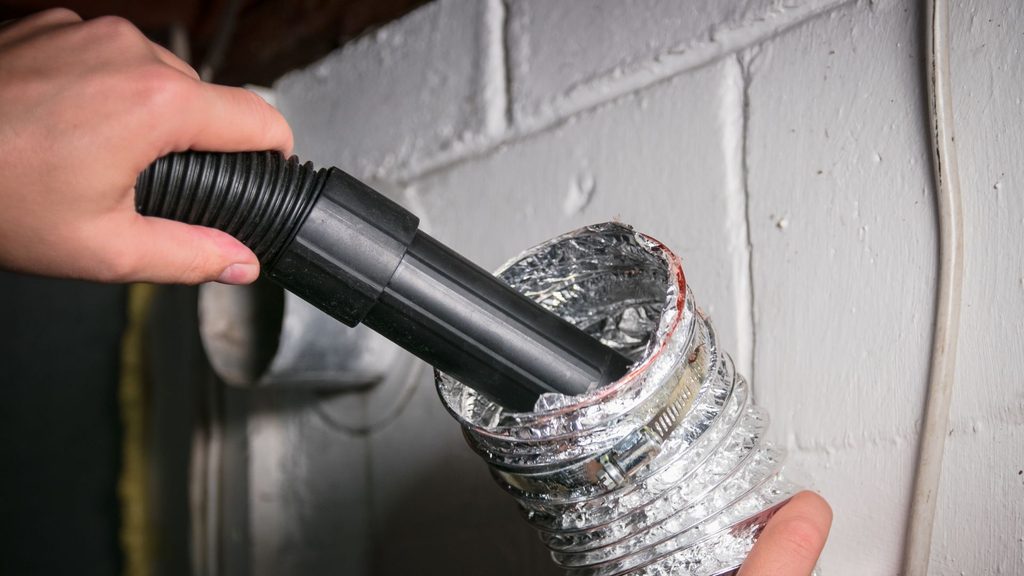 Hand inserting a vacuum hose into a dryer vent duct at the wall to remove lint
