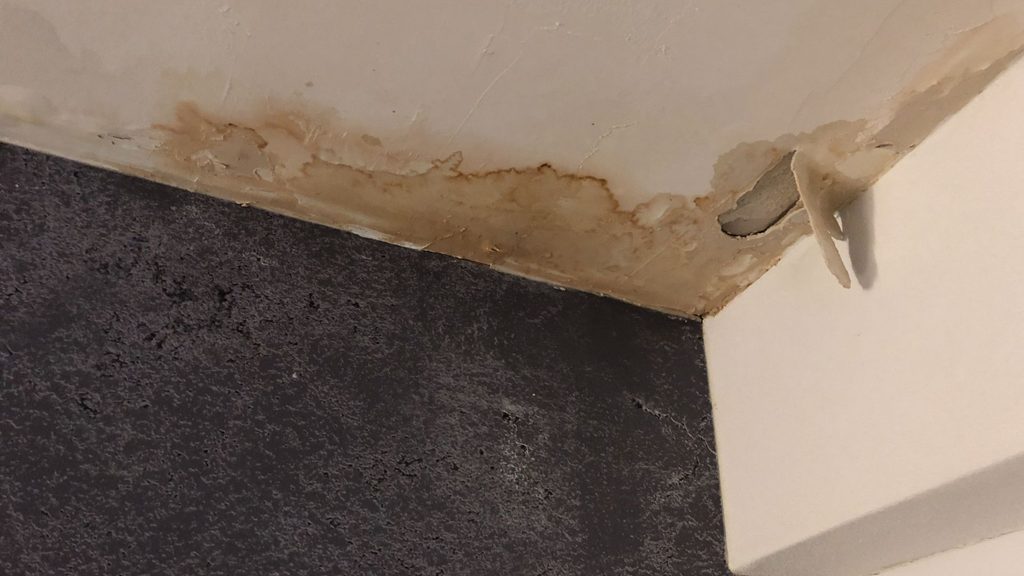water damage stain on ceiling corner with peeling and bubbling paint