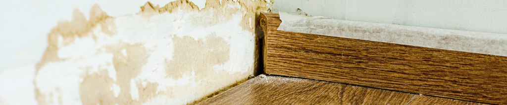 water damage stain on wall with peeling paint and warped wood floor at baseboard