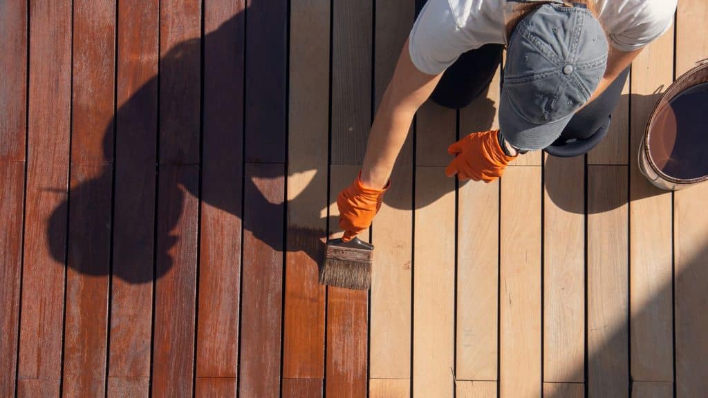Person in gloves brushing a coat of stain onto deck boards