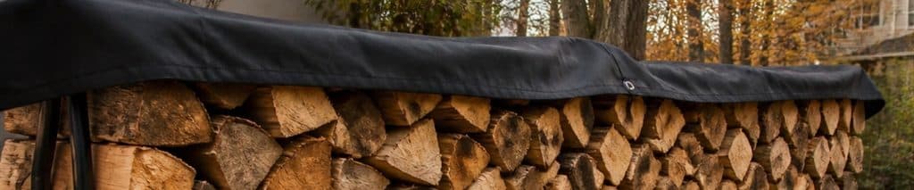 Split seasoned firewood stacked on a metal firewood rack with a cover over the top only, ready to use a firewood calculator to plan how much wood you need for winter