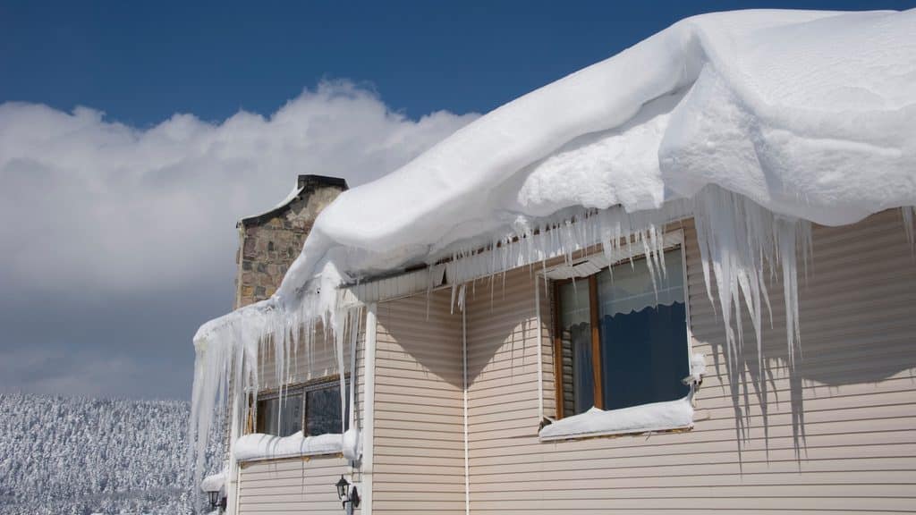 Heavy snow hanging over a roof edge with icicles, a sign to rake the roof after a storm