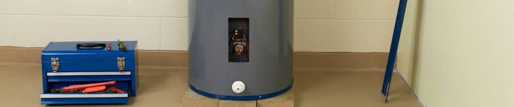 Electric tank water heater in a basement with the drain valve at the bottom and a toolbox nearby, ready to flush. How to flush a water heater