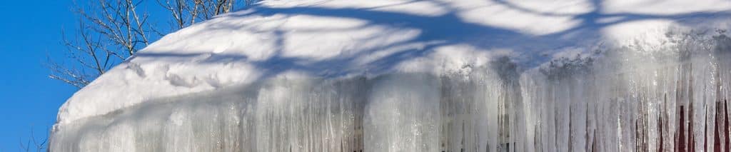 Thick icicles hanging from a snow-covered roof edge on a red house. How to prevent ice dams