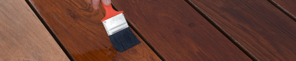 Brushing stain onto a deck board, with stained and unstained boards side by side. Stain calculator
