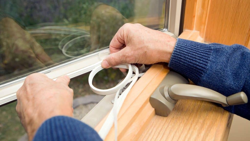 applying weatherstripping to a window to seal drafts for winter